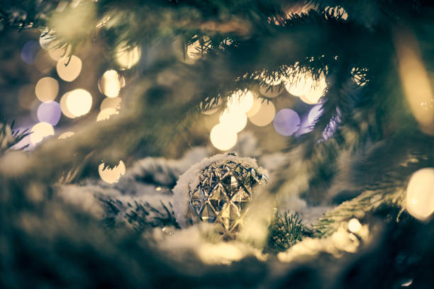 Green Christmas tree covered snow with white decorative bulb and yellow garlands lights bokeh, xmas green tree with decorative garlands. Outdoor winter holiday atmosphere festive Christmas decorations