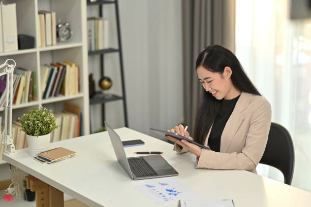 istock Smiling millennial female manager sitting in front of laptop using digital tablet checking financial data in office. 1474968646