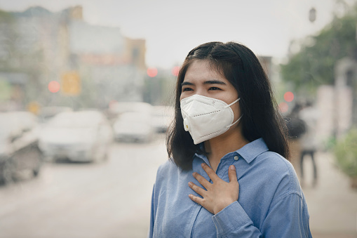 Asian woman wearing the N95 Respiratory Protection Mask against PM2.5 air pollution and headache Suffocate. City air pollution concept