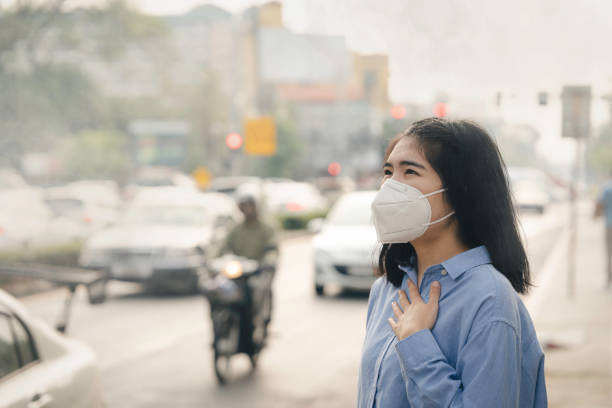 donna asiatica che indossa la maschera di protezione respiratoria n95 contro l'inquinamento atmosferico pm2.5 e mal di testa soffocare. concetto di inquinamento atmosferico della città - global warming smog city pollution foto e immagini stock