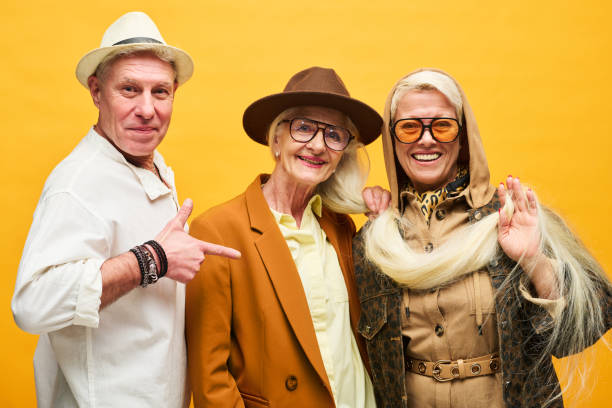 Group of happy and stylish senior people in dopamine dressing looking at camera while posing against yellow background in studio