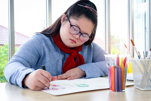 Happy children have fun study at home school, girl with down syndrome concentrate painting on paper in art classroom, education of kids with physical disability and intellectual concept