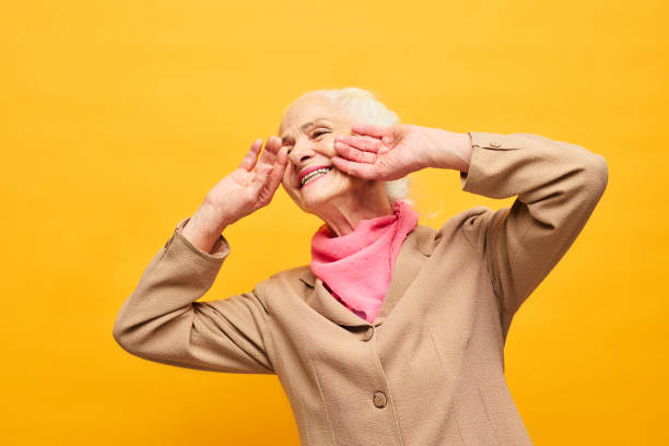 istock Senior woman in beige blazer touching face by hands while laughing 1474971486