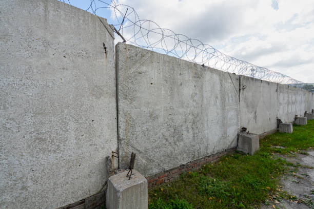 istock Concrete fence with metal barb construction on blue sky background. 1474972079