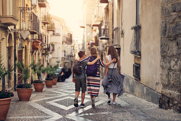 Mother and teenage kids sightseeing beautiful Italian town of Cefalu, Sicily Mother and two teenagers walking in beautiful narrow streets of Italian town of Cefalu. Sunny, off-season, Spring day in Italy, Sicily. 
Canon R5 city break stock pictures, royalty-free photos & images