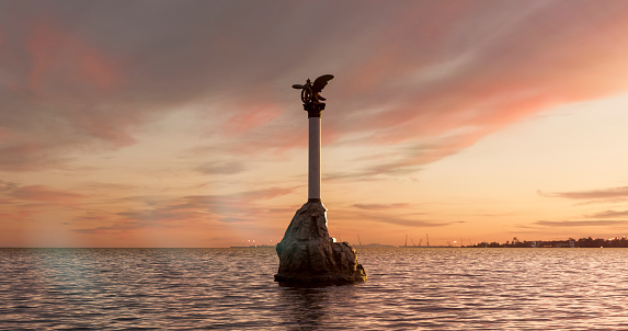 Monument to sinking ships in the Crimea during a romantic multicolored rising sky with multicolored clouds. The rising sun over the sea surface. Naval theme, Russian Navy