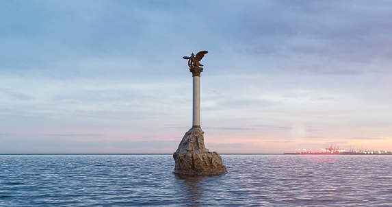 Monument to sinking ships in the Crimea during a romantic multicolored rising sky with multicolored clouds. The port can be seen in the distance. The sea surface is calm and serene