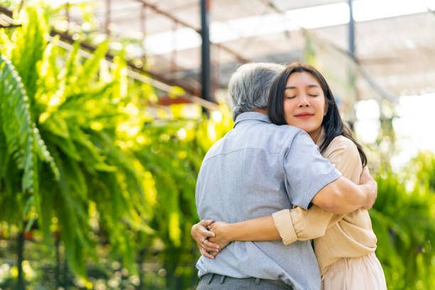 Asian woman hugging elderly father during shopping together at street market. Happy Asian family hanging out together on summer vacation. Attractive adult woman hugging elderly father during shopping at plant shop street market. Father and daughter relationship concept. father son grandfather fathers day stock pictures, royalty-free photos & images