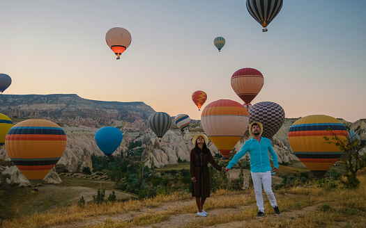 Asian women and caucasian men mid age on a trip to Kapadokya Cappadocia Turkey, a happy young couple during sunrise watching the hot air balloons of Kapadokya Cappadocia Turkey during vacation