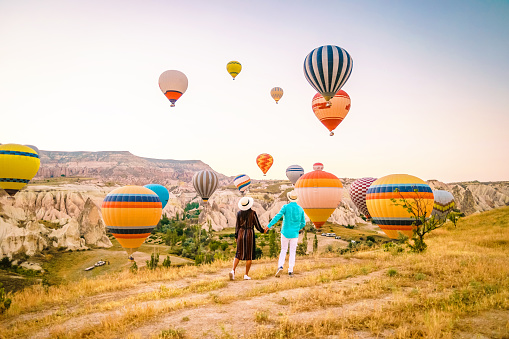 Cappadocia Turkey during sunrise, couple mid age men and woman on vacation in the hills of Goreme Capadocia Turkey, men and woman looking sunrsise with hot air balloons in Cappadocia Turkey