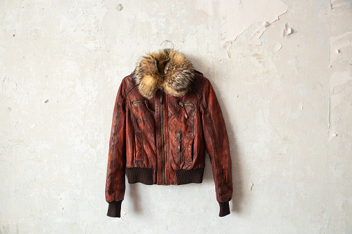 red fur leather winter women jacket hanging on a hanger on a white wall indoors