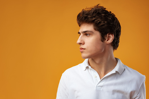 Side view of a young man looking away on yellow background close up