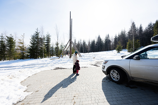 Mother holding hand daughter against big wooden swing and suv car with roof rack in mountains.