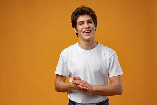 Portrait of cheerful young man clapping hands on yellow background.close up