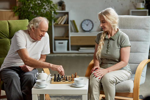Happy elderly couple, retired man and woman spending time at home, playing chess together, drinking tea. Leisure time and hobby. Concept of family, relationship, retirement, lifestyle, happiness