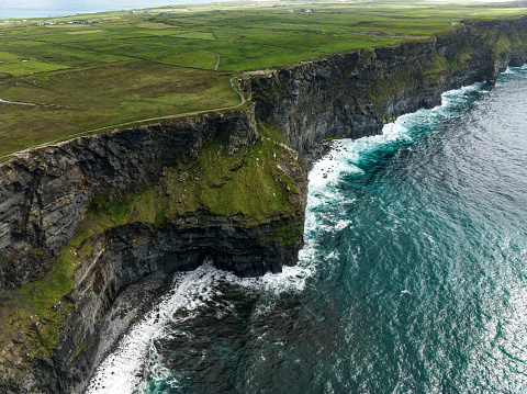 Aerial shot of the scenic Cliffs of Moher located in the County Clare, Ireland. Surrounded with green areas and the atlantic ocean.