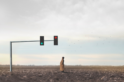 surreal woman observes the arrows of a traffic light in the middle of the desert, concept of choosing a direction in life