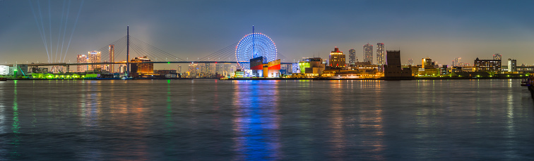 Night time panorama over the tranquil waters of the bay to the ferris wheel and port buildings of Osaka Port, Japan.