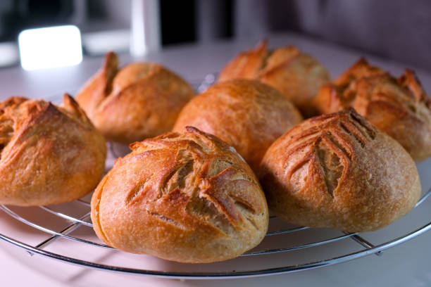 sept petits pains se tiennent sur un support juste à la sortie du four la lumière clignote lentement montrant un contour beau motif sur chacun d’eux produits de boulangerie pâtisseries fraîches pâte sans levure restaurant servant de la vitamine b - bun bread 7 grain bread dough photos et images de collection