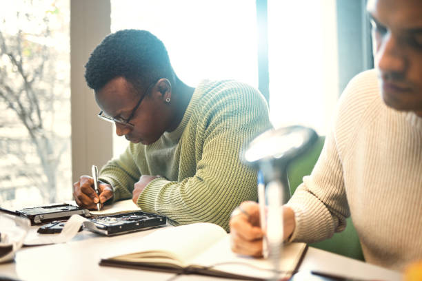 istock Students, writing or notebooks in school test, university campus exam or college degree notes in classroom library. Men, friends or people with textbook for learning, thinking education or studying 1474993813