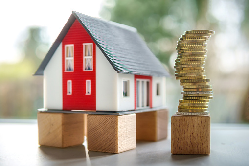 Miniature House Model with a Tower of Stacked Coins Concept for: Building, Loan Value, Renting or Buying Real Estate