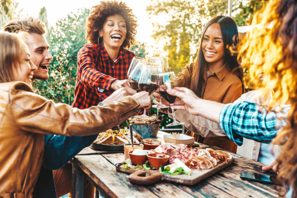 Multiracial friends having fun at barbecue dinner party in garden restaurant - Millennial people cheering red wine sitting at outside bar table - Youth lifestyle, food and beverage concept Multiracial friends having fun at barbecue dinner party in garden restaurant - Millennial people cheering red wine sitting at outside bar table - Youth lifestyle, food and beverage concept aperitif stock pictures, royalty-free photos & images