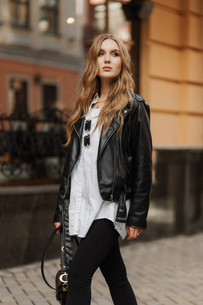 Fashionable  blonde woman model with  black leather jacket and style bag walking the city street stock photo