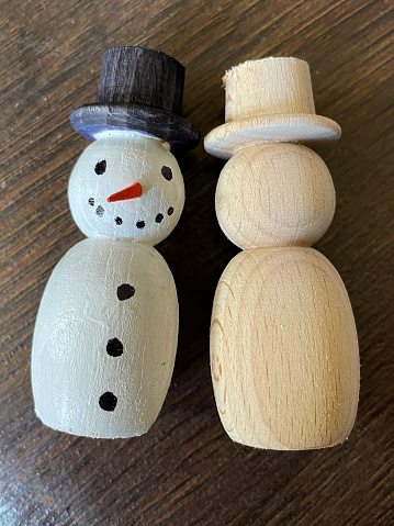 Stock photo showing a festive homemade wooden snowman decoration, cut in halves on top of a table, one half is painted and the other is unfinished, ready to be glued together