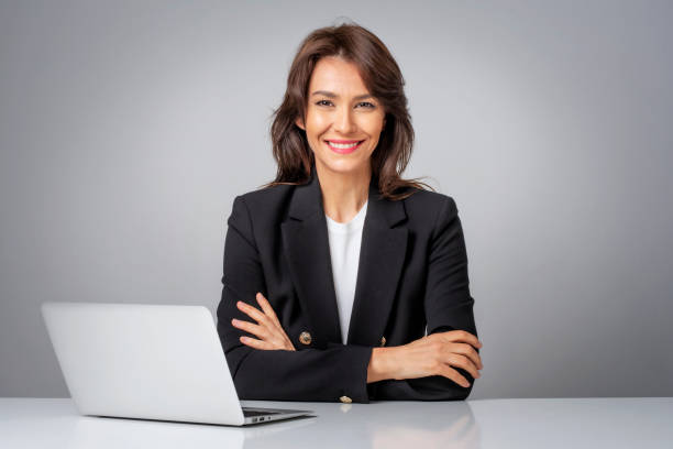 Studio portrait of a confident professional female wearing blazer and sitting with her laptop at isolated background stock photo
