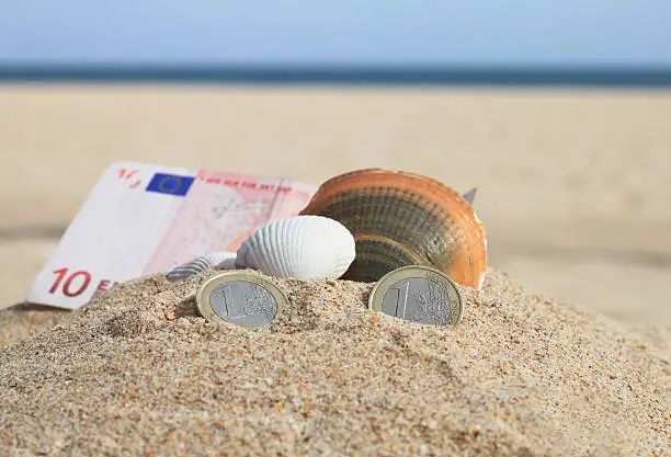 Euro coins and a ten euro bill in sand, decorated with shells, Alvor beach, Algarve, Portugal