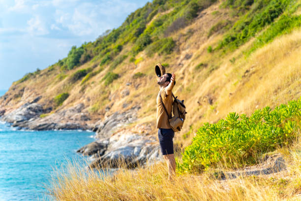 istock Caucasian man standing on coastline hill with arm raised at summer sunset. 1475004374