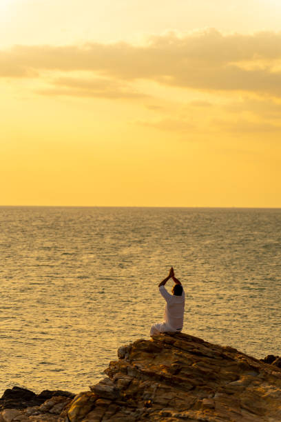 istock Caucasian man practicing meditation with ocean on coastal hill at summer sunset. 1475004458