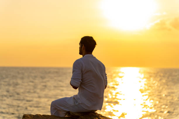 istock Caucasian man practicing meditation with ocean on coastal hill at summer sunset. 1475004493