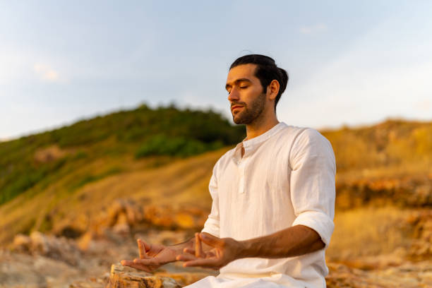 istock Caucasian man practicing meditation with ocean on coastal hill at summer sunset. 1475004547