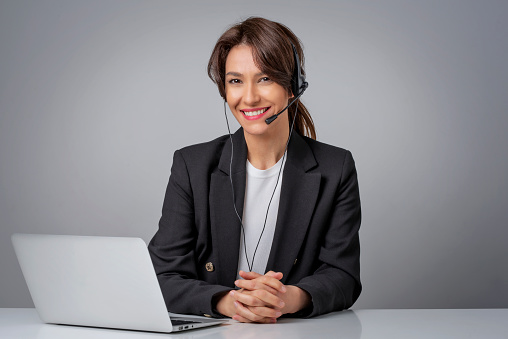 Studio shot of customer service assistant wearing headset while sitting behind her computer and working in the call center. Isolated background. Copy space.