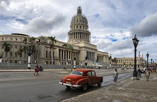 Havana, Cuba, December 9, 2017: People walk down the street in front of the National Capitol of Cuba whose cupola is being renovated. It is the seat of the Cuban parliament.