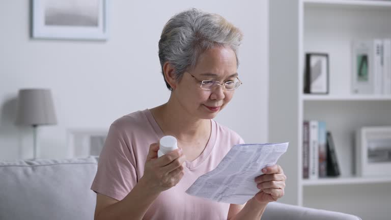 Mature Asian woman reading medical instructions before taking medicine.