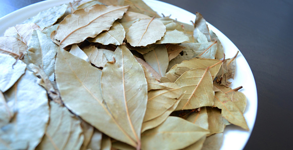 photo of a white plate with bay leaves on a dark wood background, spices and seasonings, dried plants