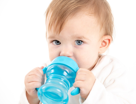 Stock studio photo with a white background of a baby drinking water from a canteen with handles.