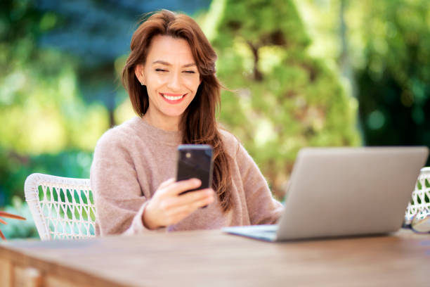 istock Happy middle aged woman using a smartphone and laptop while relaxing outdoor 1475010503