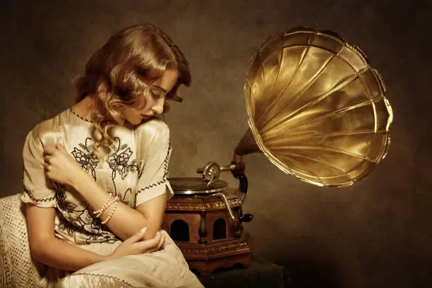 Retro woman sitting and listening to music on gramophone - added real film grain and brown tone for the mood.