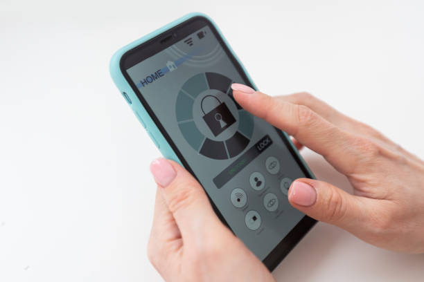 istock Young woman holding smart phone with launched security application at home. Concept of controlling and managing home security from a mobile device. 1475011035