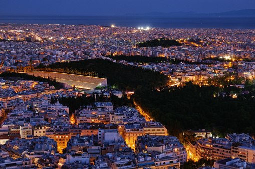 Night view of Athens, Greece with ancient and restored Panathenaic stadium of Kallimarmaro, shot form hill of Lycabettus. Beautiful city at blue hour, iconic site for Olympic games movement. National Garden in center of city.