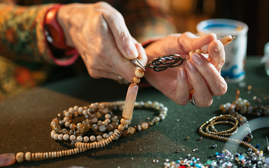 Close up of unrecognizable woman stringing beads in a workshop.