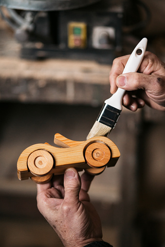 Close up of unrecognizable carpenter putting protective varnish on wooden car toy in a workshop.