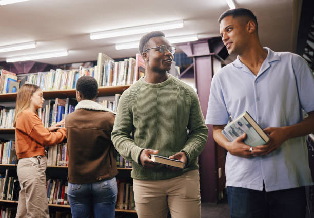 istock Education, students or friends in library at university, college or school learning, talking or studying. Studying, scholarship or young men with books for knowledge growth or future development 1475012890