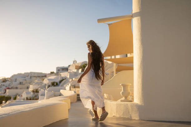 Mulher asiática fêmea nova com vestido branco em férias em Santorini, apreciando a vista da arquitetura tradicional - foto de acervo