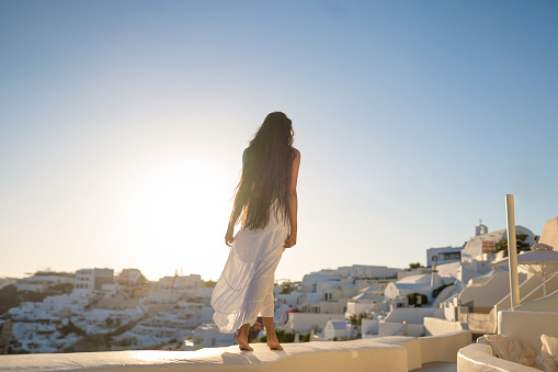 Young female asian woman with white dress on a vacation in Santorini, enjoying the view of the traditional architecture