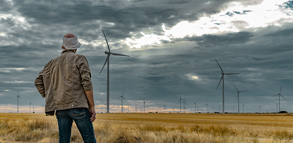 Castilla y León, Spain. Rear view of man whit hat looking far a large amount of wind power towers in cloudy and windy afternoon