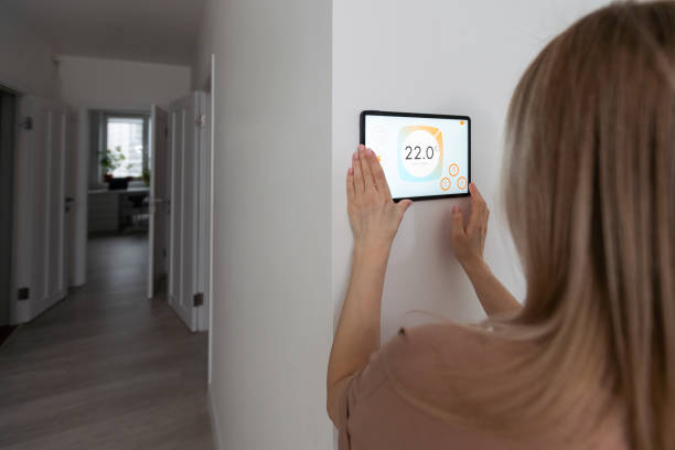 istock Woman controlling home with a digital touch screen panel installed on the wall in the living room 1475016691